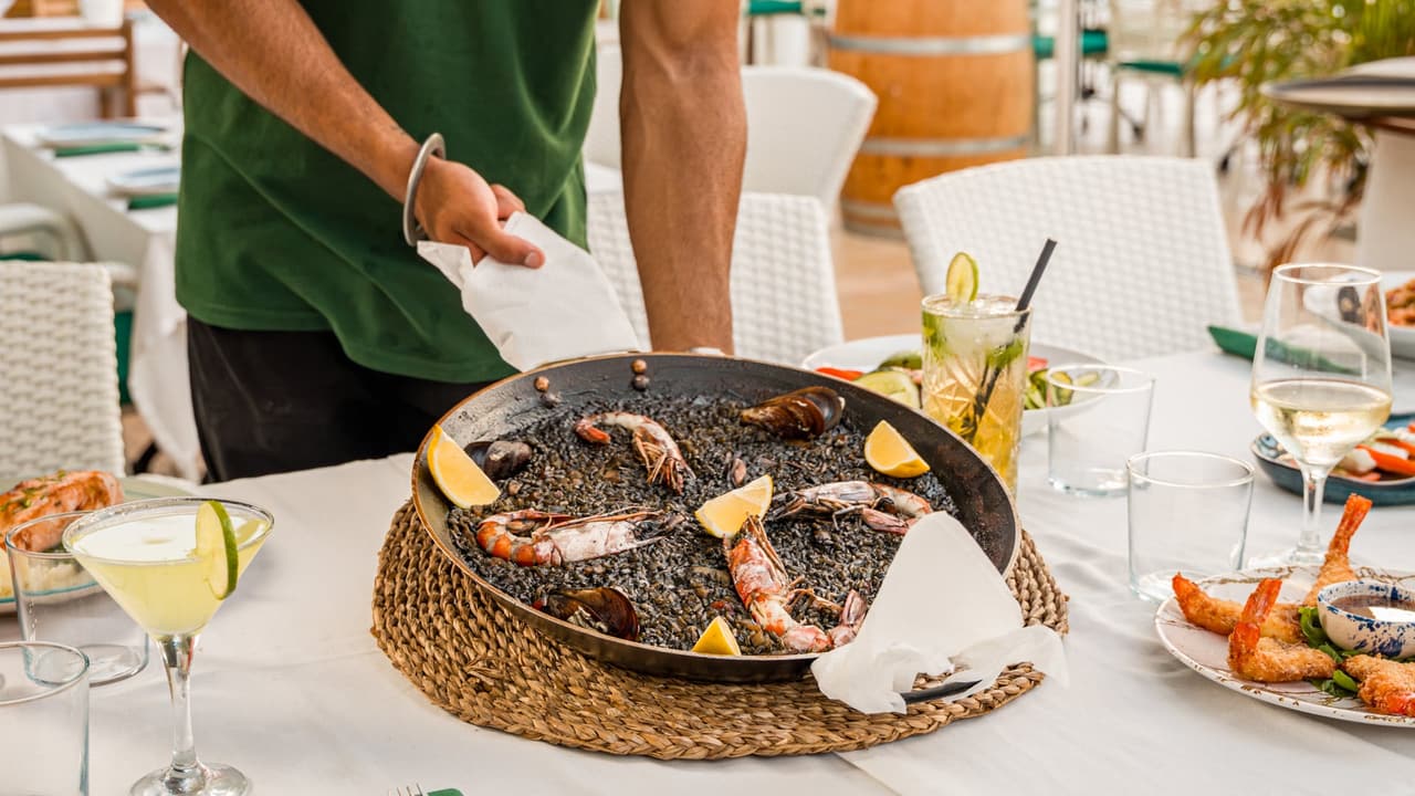 Schwarze Meeresfrüchte-Paella, serviert auf der Terrasse des Casanova Restaurante am Meer in Cala Estancia